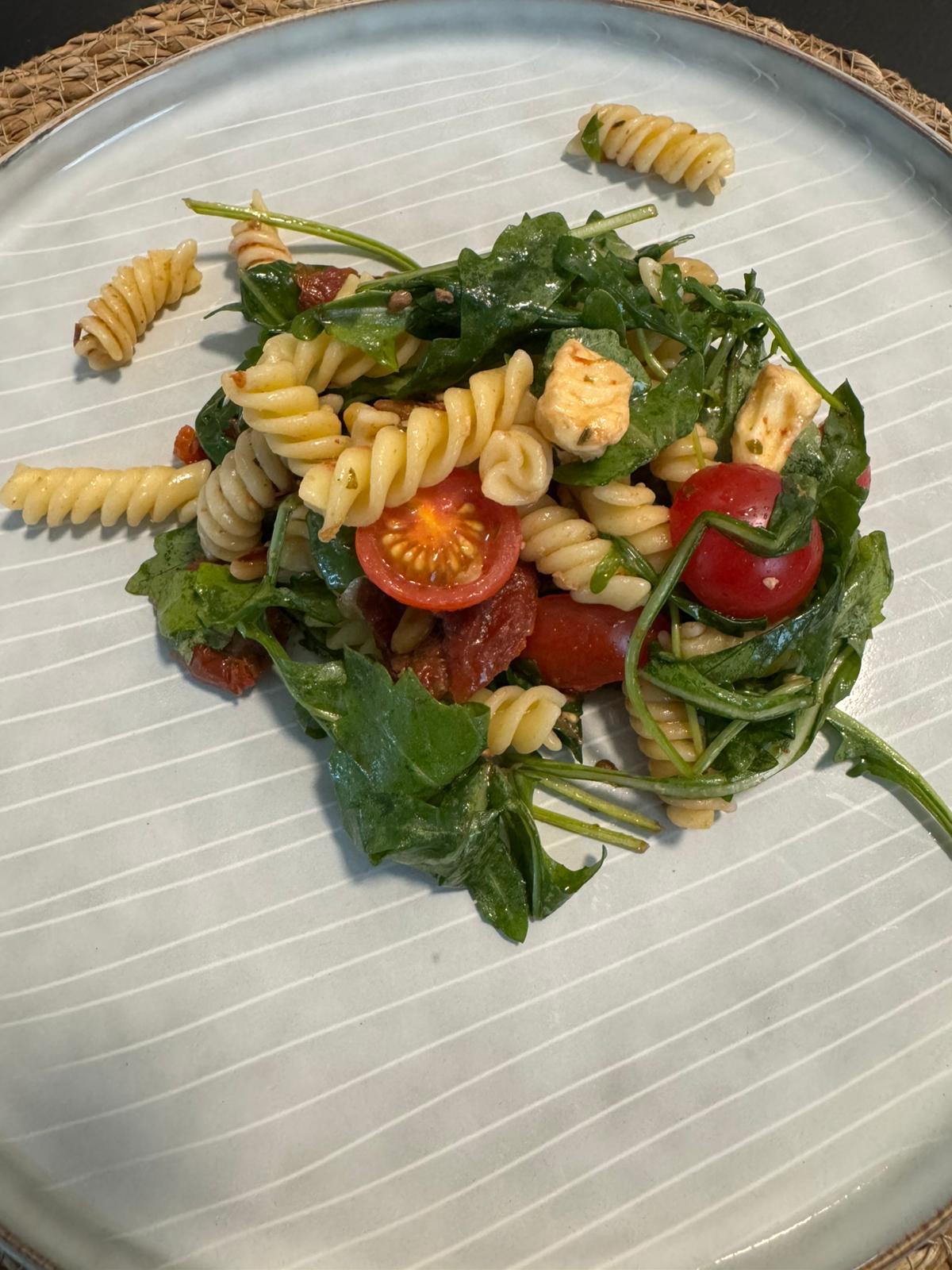 Mediterraner Nudelsalat mit Rucola, Mozzarella, Cherry-Tomaten und Pinienkernen in einer großen Schüssel