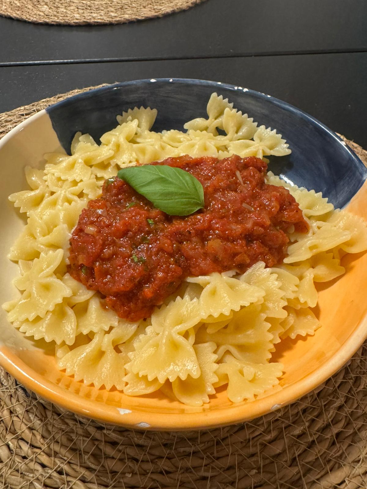 Nudeln mit roter Tomatensauce in einem tiefen Teller, garniert mit frischem Basilikum