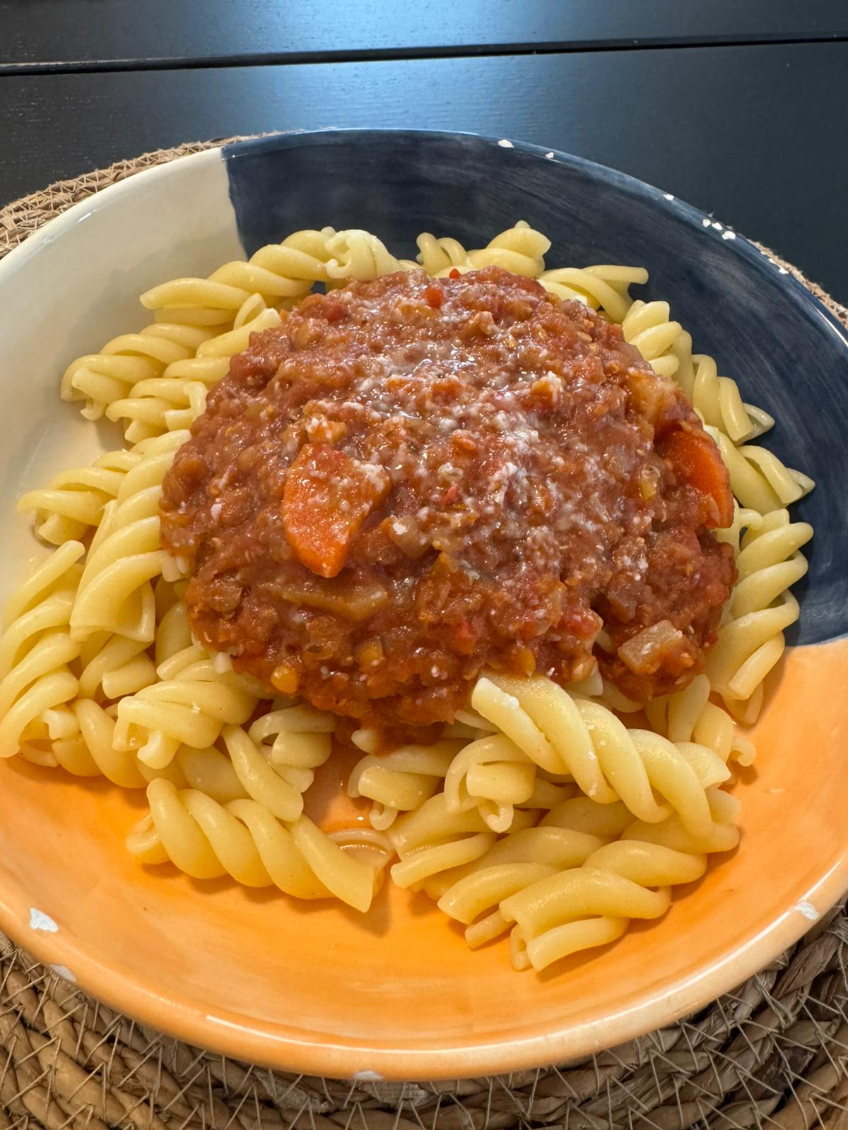 Nudeln mit vegetarischer Linsenbolognese in einem tiefen Teller, garniert mit frischem Thymian