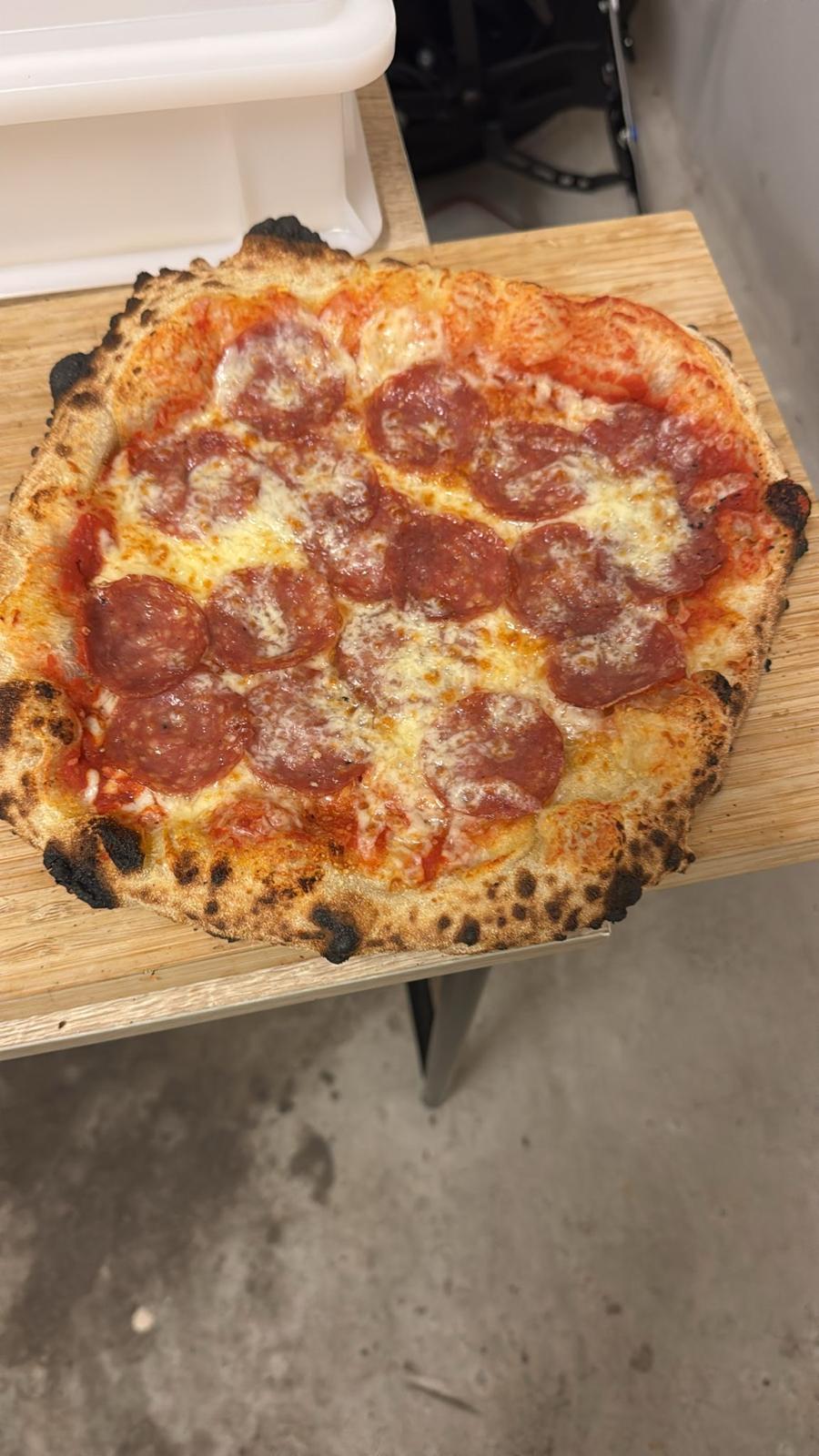 Neapolitanische Pizza mit Salami und charakteristischem Leoparding-Rand auf einem Holzbrett